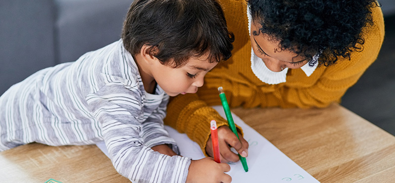 A mother and her young son coloring together at home. 