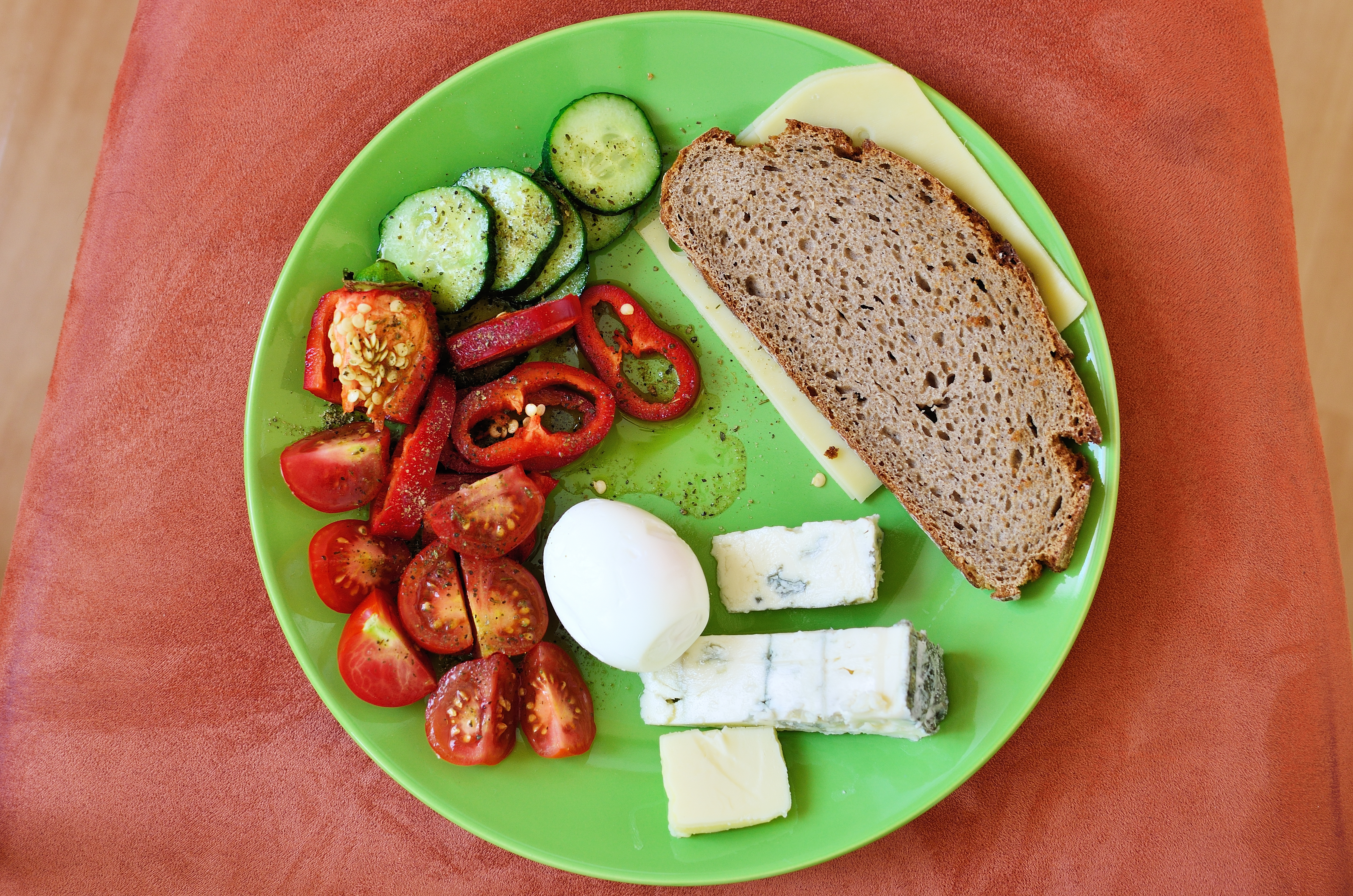 A snack plate consisting of tomatoes, cucumbers, peppers, a boiled egg, cheese and a piece of whole grain bread
